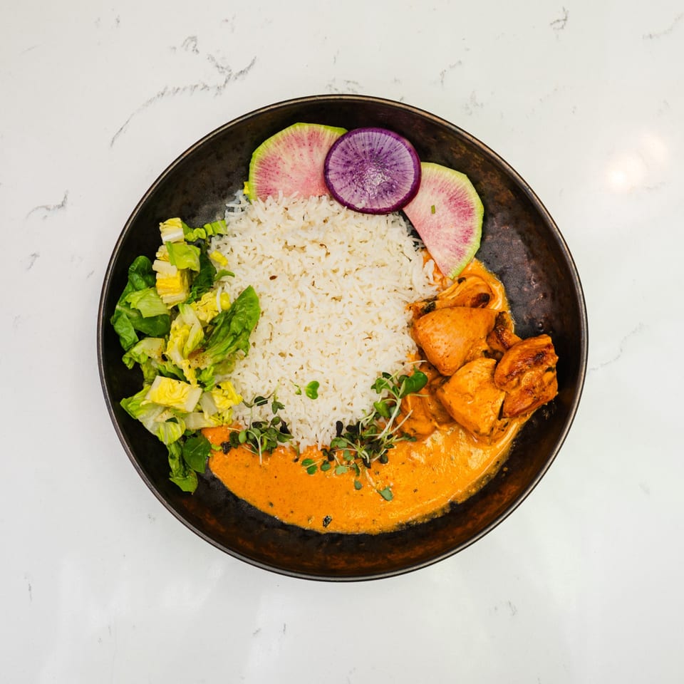 Indian butter chicken with rice, salad, and watermelon radish slices in a dark bowl.