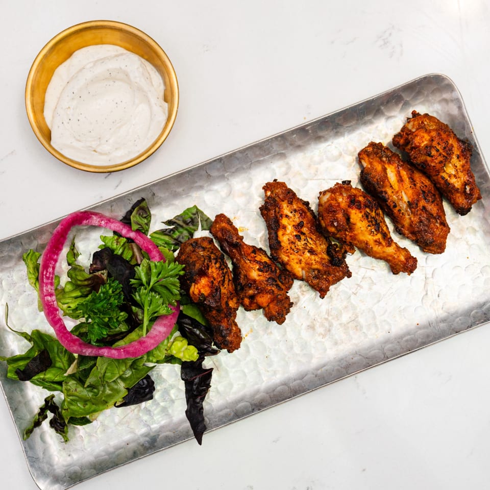 Indian spiced chicken wings with a side salad and a bowl of creamy white dipping sauce.