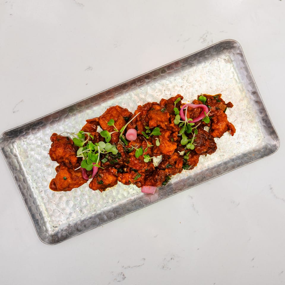 Indian chicken pakora, garnished with microgreens and pickled red onions, on a hammered metal tray.